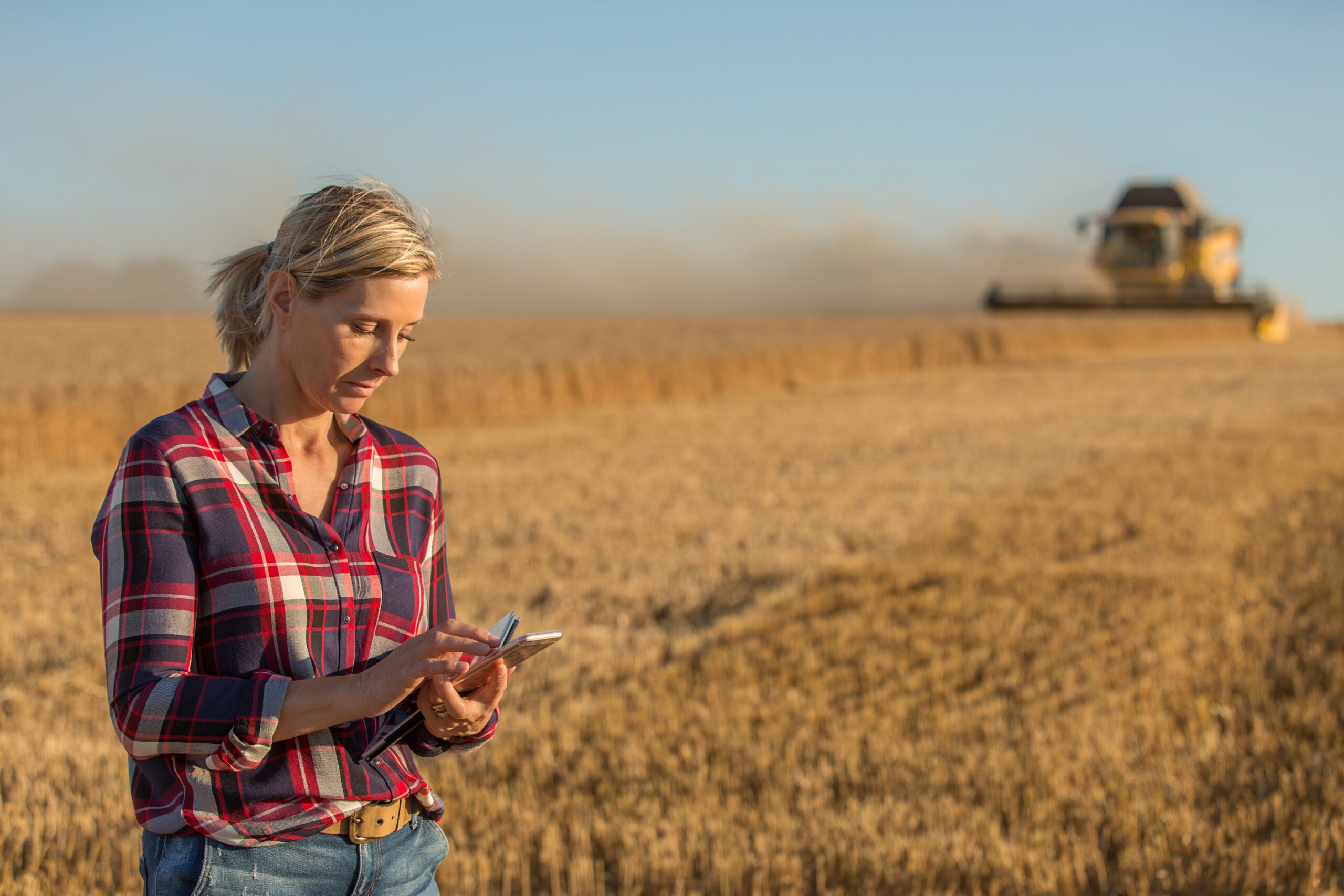 A young farmer looks at his phone walking away from a truck driver in the field.